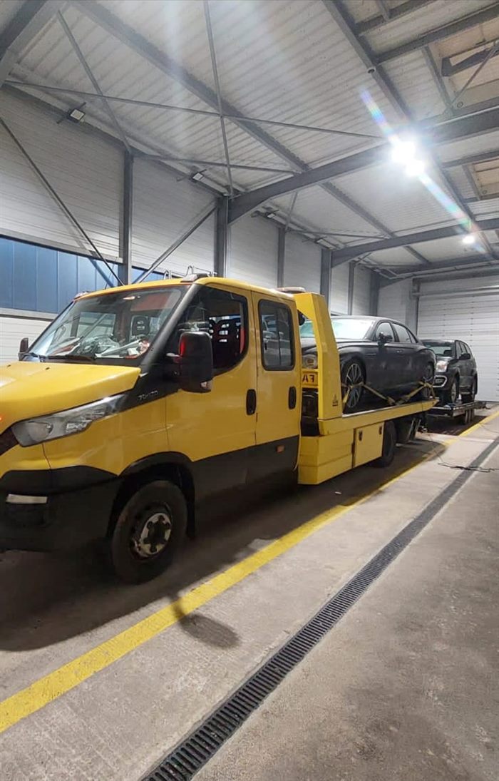 Recovery truck with a car loaded on the bed, parked in a depot at night